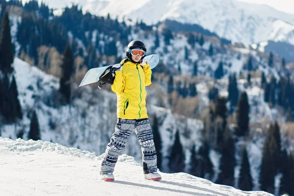 Молодая Женщина Сноубордистка Ходит Лыжному Склону Держа Сноуборд Плечах Смотрит — стоковое фото