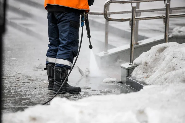 Worker cleaning driveway with gasoline high pressure washer splashing the dirt, asphalt road border. High pressure cleaning