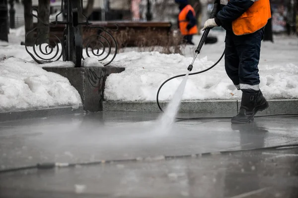 Worker cleaning driveway with gasoline high pressure washer splashing the dirt, asphalt road border. High pressure cleaning