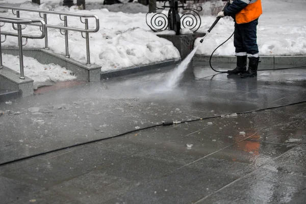 Worker cleaning driveway with gasoline high pressure washer splashing the dirt, asphalt road border. High pressure cleaning