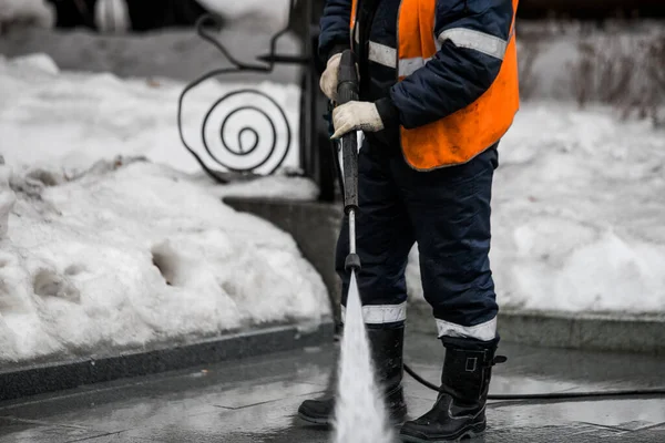 Worker cleaning driveway with gasoline high pressure washer splashing the dirt, asphalt road border. High pressure cleaning