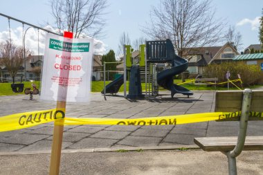 Bir COVID-19 kapalı oyun alanı uyarısı arka planda bir park bankına bantlanmış.