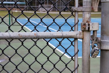 Arka planda ağ olan bir tenis kortunun asma kilitli kapısını kapatın..