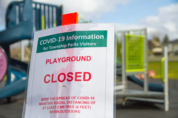 Ein Geschlossenes Spielplatzschild Für Covid Vor Einem Kleinen Kinderspielplatz lizenzfreie Stockfotos