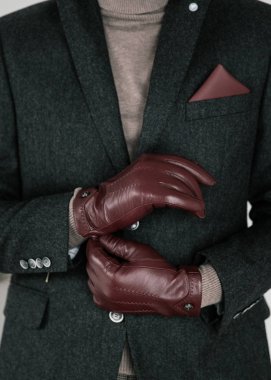 Şık giyimli, sakallı bir iş adamı şık bir takım elbise, kahverengi ayakkabılar, kravat, eldivenler, pahalı bir dairede poz veren bir adam.