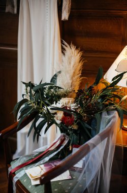 Ahşap bir gardıropta şık ve pahalı bir gelinlik ve gelin buketi.