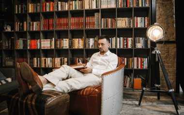 Hafif takım elbiseli şık damat kütüphanede gelinine aşk mektubu yazıyor.