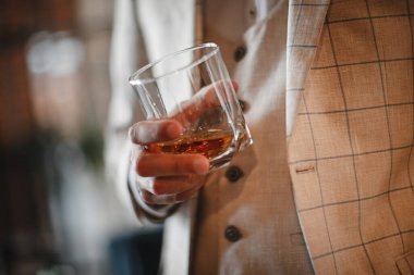 Hafif takım elbiseli şık bir damat elinde viskiyle poz veriyor.