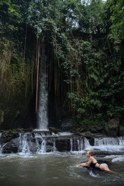 Bali adasında Endonezya 'ya seyahat ederken mayo giymiş sarışın bir blog yazarı vahşi bir şelalede cinsel olarak poz veriyor.
