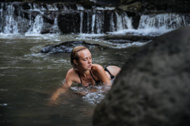 Bali adasında Endonezya 'ya seyahat ederken mayo giymiş sarışın bir blog yazarı vahşi bir şelalede cinsel olarak poz veriyor.