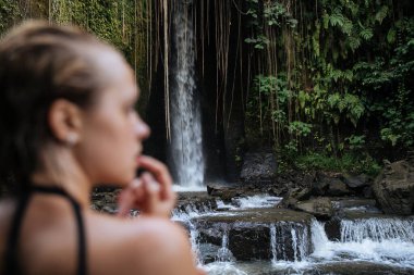 Bali adasında Endonezya 'ya seyahat ederken mayo giymiş sarışın bir blog yazarı vahşi bir şelalede cinsel olarak poz veriyor.