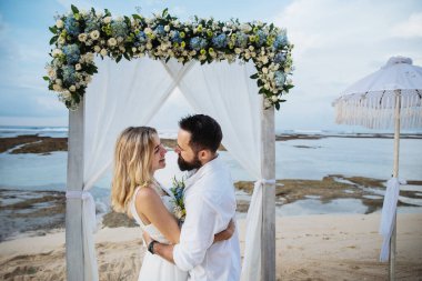 Birbirine aşık çiftler - gelin ve damat düğün günlerinde okyanus kenarında, Endonezya 'nın egzotik Asya adası Bali' de sarılıp öpüşürler. 