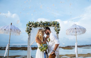 couple in love - bride and groom on their wedding day hug and kiss on the beach near the ocean on the exotic Asian island of Bali in Indonesia  clipart