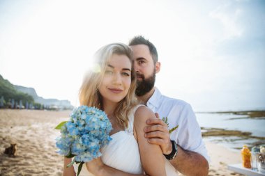 Birbirine aşık çiftler - gelin ve damat düğün günlerinde okyanus kenarında, Endonezya 'nın egzotik Asya adası Bali' de sarılıp öpüşürler. 