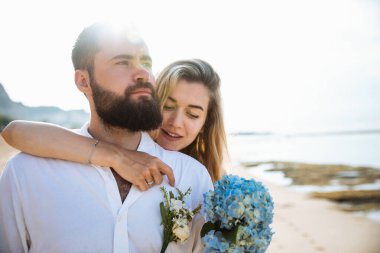Birbirine aşık çiftler - gelin ve damat düğün günlerinde okyanus kenarında, Endonezya 'nın egzotik Asya adası Bali' de sarılıp öpüşürler. 