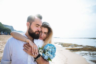 Birbirine aşık çiftler - gelin ve damat düğün günlerinde okyanus kenarında, Endonezya 'nın egzotik Asya adası Bali' de sarılıp öpüşürler. 