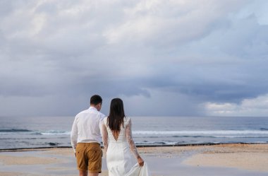 Birbirine aşık çiftler - gelin ve damat düğün gününde okyanusun kıyısında, Endonezya 'nın egzotik Asya adası Bali' de kucaklaşıp öpüşürler, inanılmaz manzara