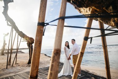 Birbirine aşık çiftler - gelin ve damat düğün gününde okyanusun kıyısında, Endonezya 'nın egzotik Asya adası Bali' de kucaklaşıp öpüşürler, inanılmaz manzara