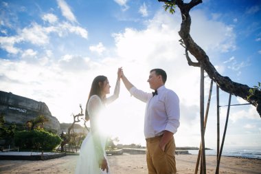 Birbirine aşık çiftler - gelin ve damat düğün gününde okyanusun kıyısında, Endonezya 'nın egzotik Asya adası Bali' de kucaklaşıp öpüşürler, inanılmaz manzara