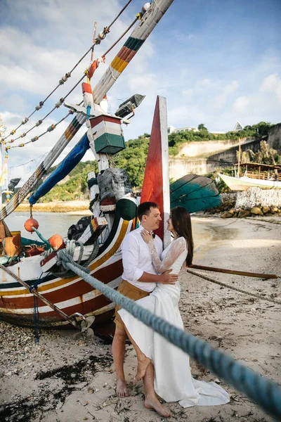 恋人同士 結婚式の日に新郎新婦抱擁し インドネシアのバリのエキゾチックなアジアの島の海でビーチでキス 信じられないほどの風景 明るい漁船 — ストック写真