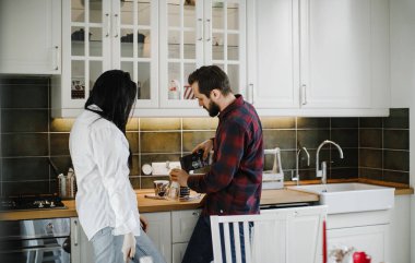 Pijamalı karı koca şaka yapıyor ve şık bir mutfakta kahve yapıyorlar.