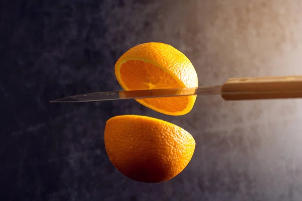 Knife and orange cut are frozen in mid air