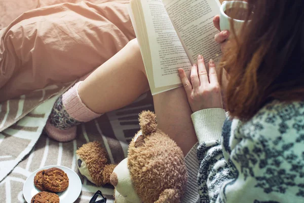 Chica leyendo libro en la cama con calcetines calientes beber café —  Fotos de Stock