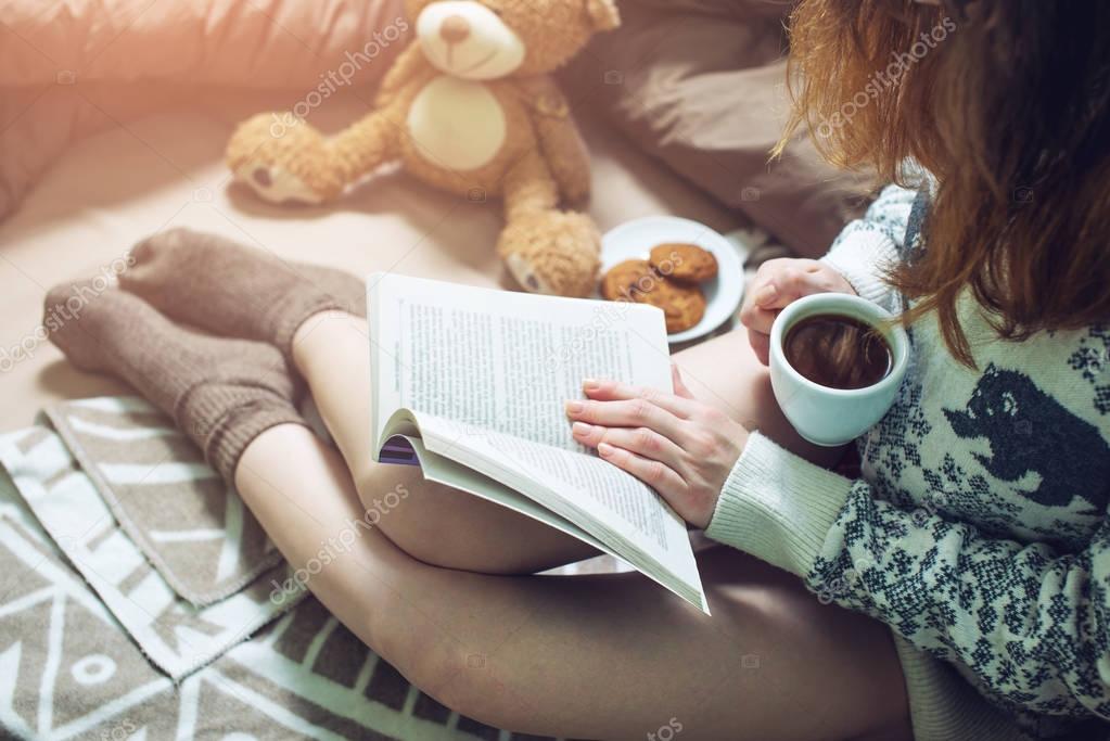 girl reading book in bed with warm socks drinking coffee