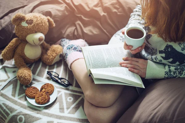 Дівчина читає книгу в ліжку з теплими шкарпетками п'є каву — стокове фото