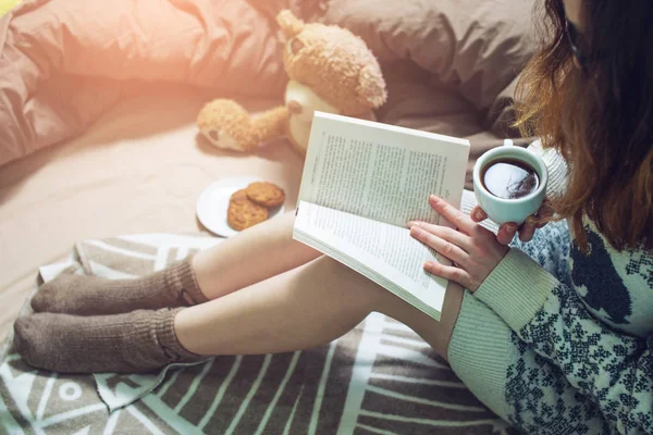 Chica leyendo libro en la cama con calcetines calientes beber café —  Fotos de Stock