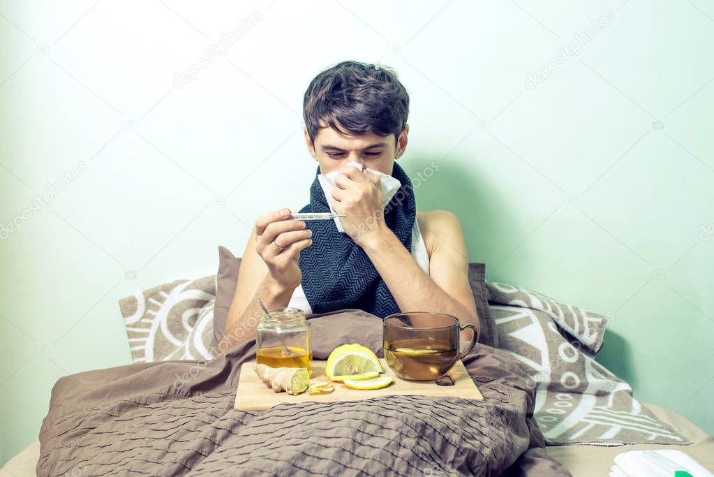 young man lies in bed sick with colds and flu
