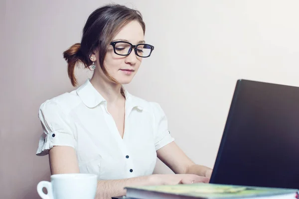 Chica atractiva con las gafas de escribir en un ordenador portátil —  Fotos de Stock