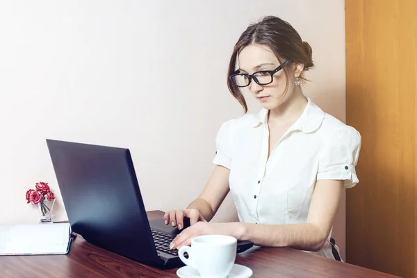 Chica atractiva con las gafas de escribir en un ordenador portátil — Foto de Stock