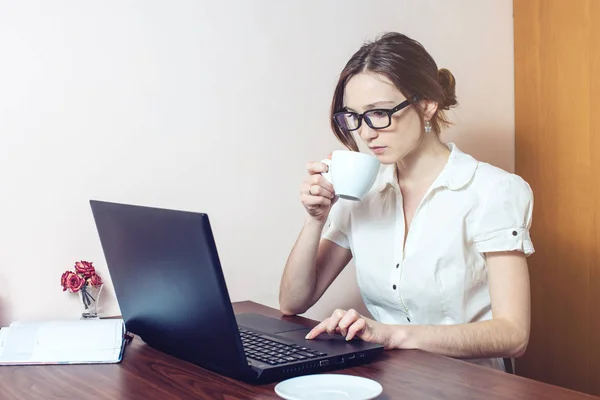 Chica atractiva con las gafas de escribir en un ordenador portátil — Foto de Stock