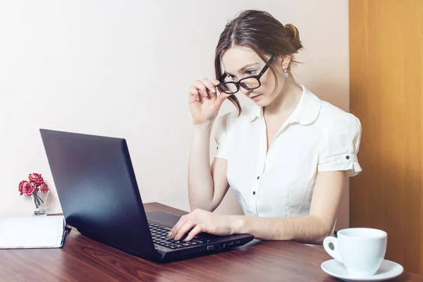 Chica atractiva con las gafas de escribir en un ordenador portátil — Foto de Stock