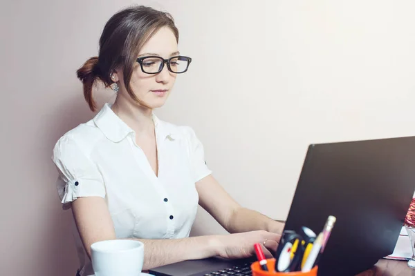 Chica atractiva con las gafas de escribir en un ordenador portátil —  Fotos de Stock