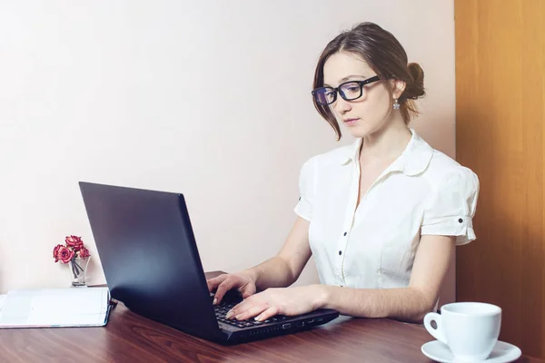 Chica atractiva con las gafas de escribir en un ordenador portátil — Foto de Stock