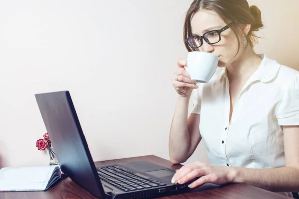 Chica atractiva con las gafas de escribir en un ordenador portátil — Foto de Stock