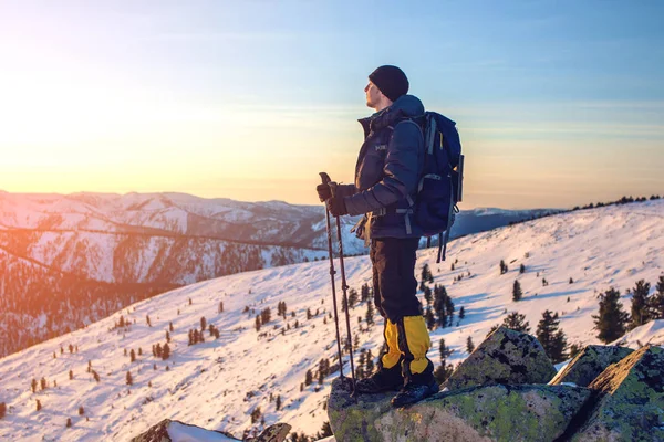 Mannen vandrare stående på snötäckta bergstopp i solnedgången — Stockfoto