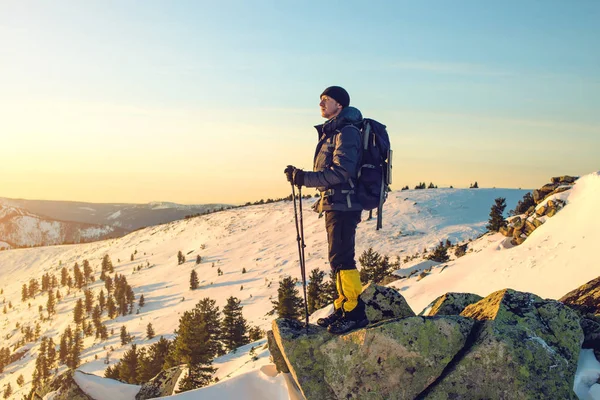 Mannen vandrare stående på snötäckta bergstopp i solnedgången — Stockfoto