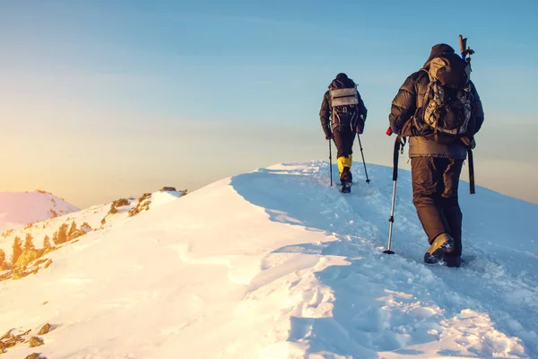 Πεζοπόροι που ταξιδεύει στα χιονισμένα βουνά στην κορυφή στο ηλιοβασίλεμα — Φωτογραφία Αρχείου