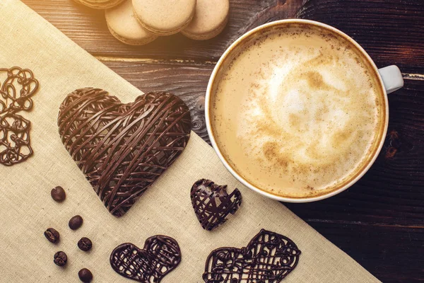 Cappuccino café com espuma bonita próxima macarons e coração de chocolate . — Fotografia de Stock