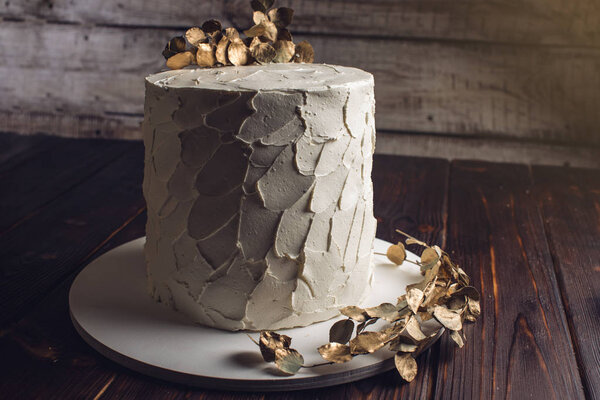 white cream cake decorated with a branch with gold leaves