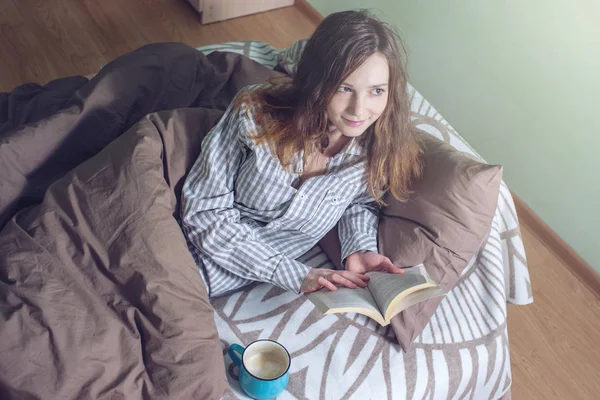Cute girl reading a book while lying in bed