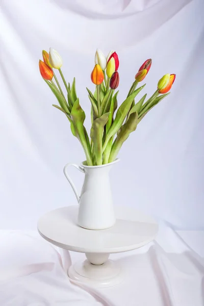 Tulipanes en un jarrón blanco sobre fondo de tela ondulada blanca —  Fotos de Stock