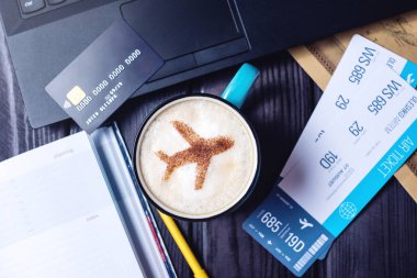 Dizüstü bilgisayar, uçak biletleri, kahve, kredi kartı masada yatıyor.