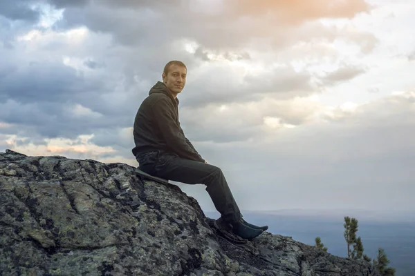男は丘の中腹に石に座って、手の高さから景色を眺めて、自由を楽しんでいます — ストック写真