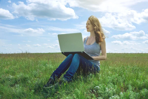 Femme assise sur une prairie verte sur le fond du ciel avec des nuages et travailler ou étudier avec un ordinateur portable sans fil — Photo