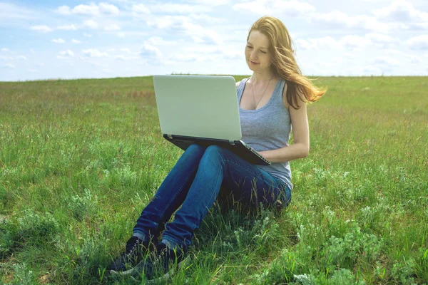 Femme assise sur une prairie verte sur le fond du ciel avec des nuages et travailler ou étudier avec un ordinateur portable sans fil — Photo