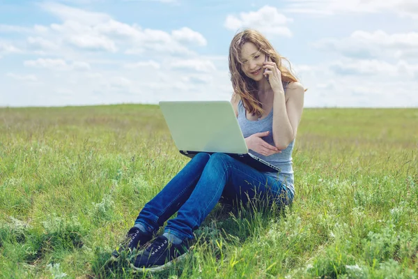 Femme assise sur une prairie verte sur le fond du ciel avec des nuages et travailler ou étudier avec un ordinateur portable sans fil — Photo